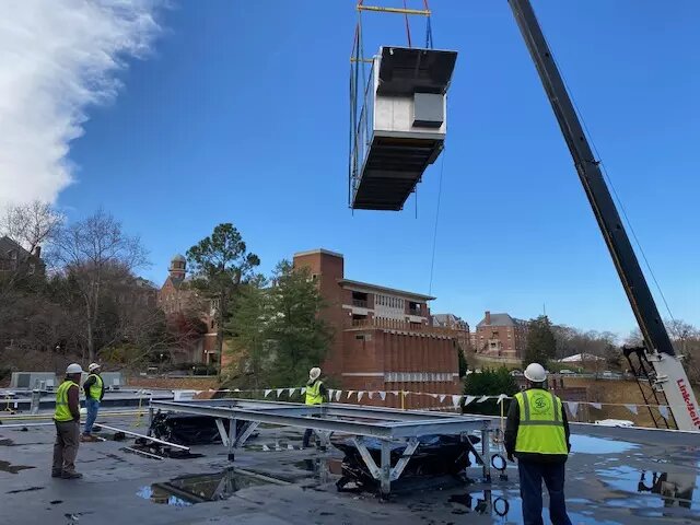 A Southern Air crew lowering a large HVAC unit through a building roof by crane on a commercial job site in Virginia
